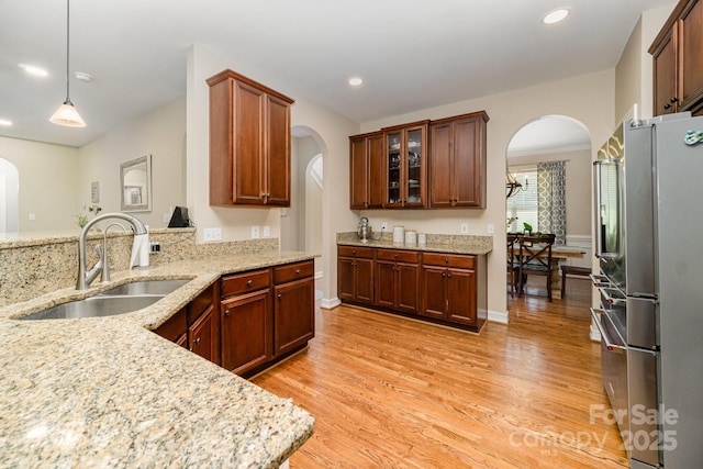 kitchen featuring sink, stainless steel refrigerator, pendant lighting, light stone countertops, and light hardwood / wood-style floors