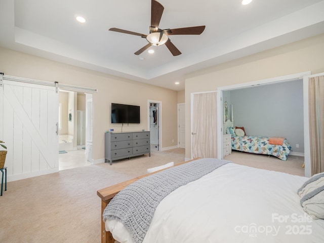 bedroom featuring a raised ceiling, connected bathroom, a barn door, and ceiling fan