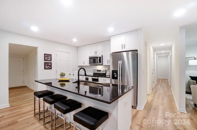 kitchen with white cabinetry, sink, stainless steel appliances, a kitchen island with sink, and light wood-type flooring