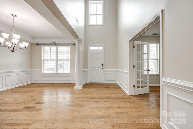 foyer with ornamental molding, a chandelier, decorative columns, and light hardwood / wood-style flooring