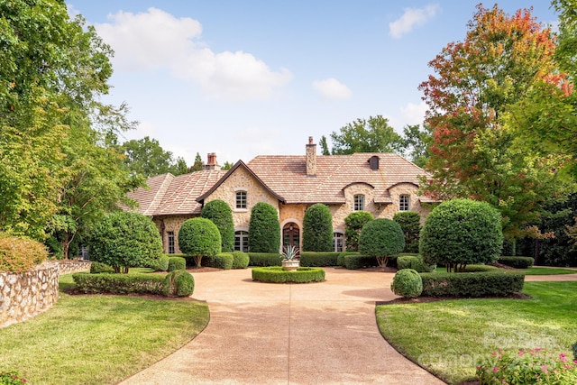 view of front of home with a chimney, stone siding, curved driveway, and a front yard