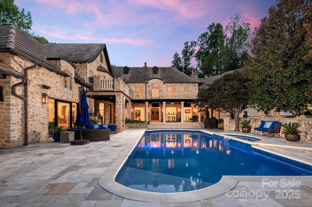 pool at dusk featuring an in ground hot tub, an outdoor hangout area, and a patio area