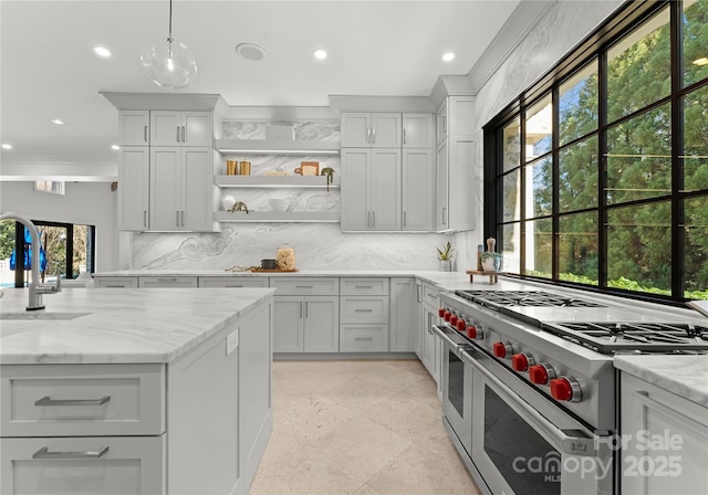 kitchen featuring pendant lighting, sink, decorative backsplash, range with two ovens, and light stone countertops