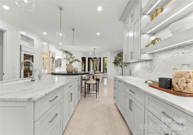 kitchen featuring a spacious island, a chandelier, hanging light fixtures, light stone countertops, and backsplash