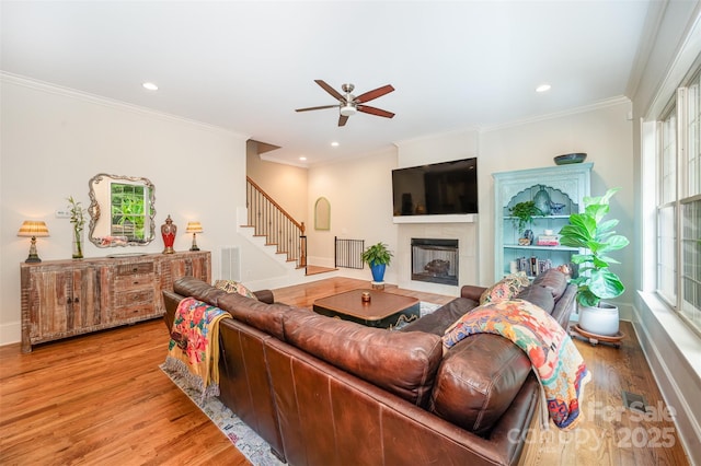 living room featuring a tiled fireplace, ceiling fan, light hardwood / wood-style flooring, and ornamental molding