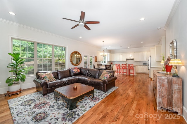 living room with ceiling fan with notable chandelier, light wood-type flooring, and crown molding