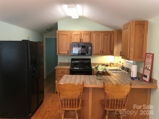 kitchen featuring lofted ceiling, kitchen peninsula, light hardwood / wood-style flooring, black appliances, and tile countertops