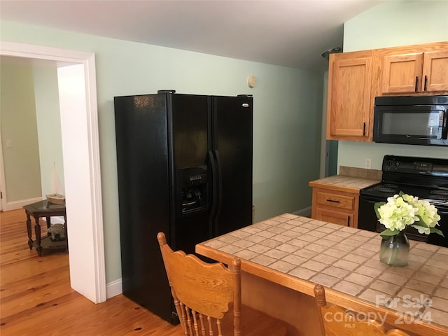 kitchen with black appliances, light hardwood / wood-style floors, and tile counters