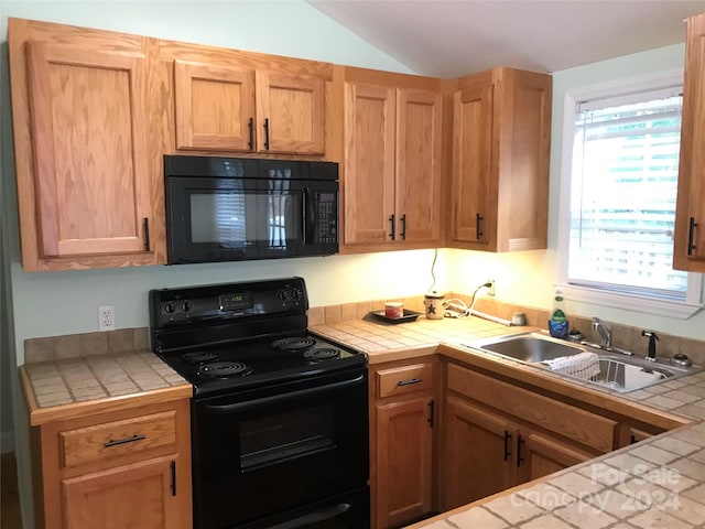 kitchen featuring black appliances, lofted ceiling, sink, and tile countertops