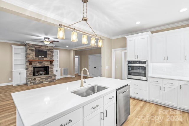 kitchen with sink, white cabinets, stainless steel appliances, a stone fireplace, and ceiling fan