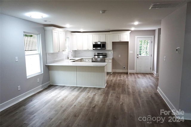 kitchen with appliances with stainless steel finishes, white cabinets, kitchen peninsula, dark hardwood / wood-style flooring, and sink