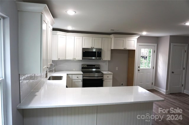 kitchen with sink, white cabinetry, kitchen peninsula, stainless steel appliances, and dark hardwood / wood-style flooring