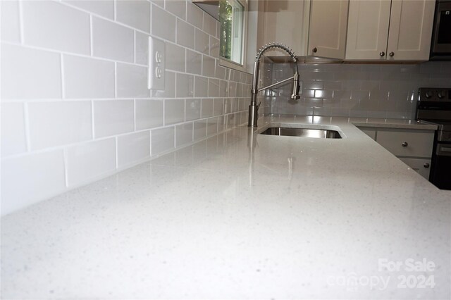 kitchen with light stone countertops, backsplash, electric range, and sink