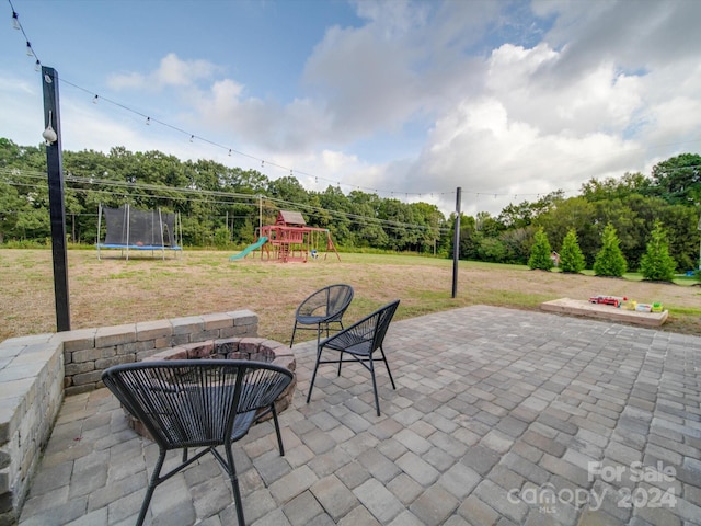 view of patio featuring a trampoline, a playground, and a fire pit