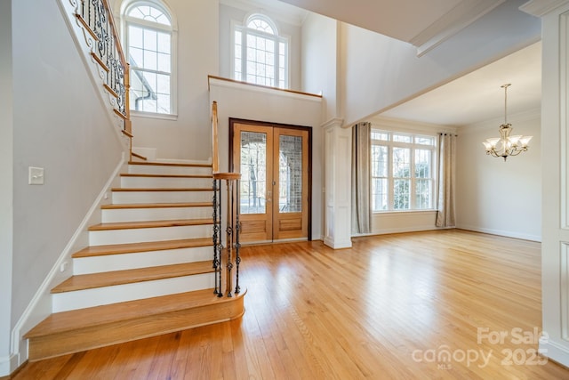 entrance foyer featuring a chandelier, a high ceiling, ornamental molding, light wood-type flooring, and french doors