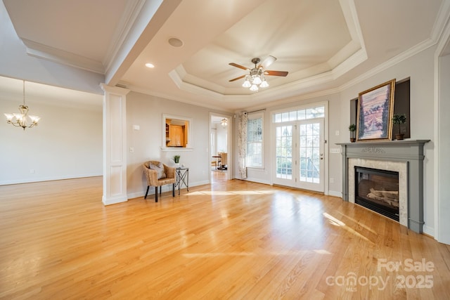 unfurnished living room with wood-type flooring, ornamental molding, a tray ceiling, a tile fireplace, and ceiling fan with notable chandelier