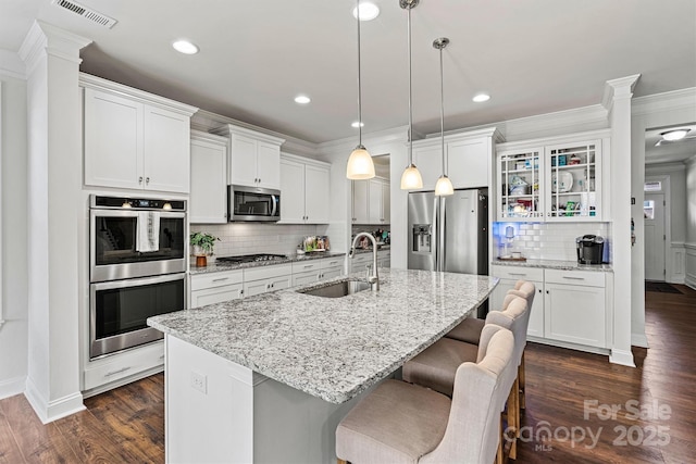 kitchen with stainless steel appliances, visible vents, dark wood-type flooring, a sink, and an island with sink