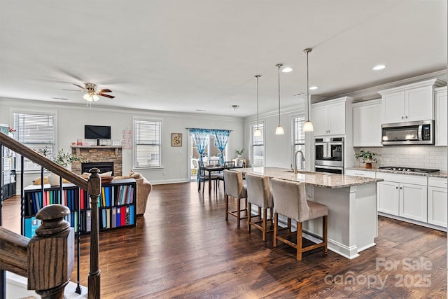 kitchen with dark wood finished floors, a center island with sink, appliances with stainless steel finishes, open floor plan, and a kitchen breakfast bar