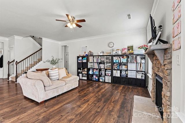 living area with ceiling fan, a stone fireplace, wood finished floors, stairway, and crown molding