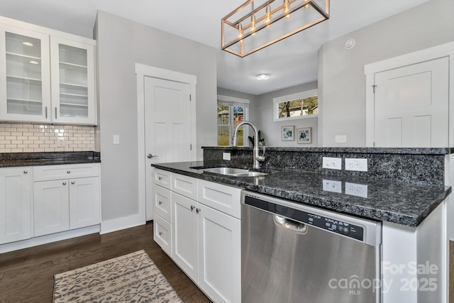 kitchen featuring stainless steel dishwasher, dark stone counters, sink, white cabinets, and hanging light fixtures