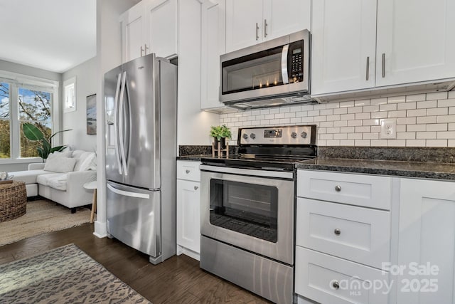 kitchen featuring appliances with stainless steel finishes, tasteful backsplash, dark wood-type flooring, dark stone countertops, and white cabinetry