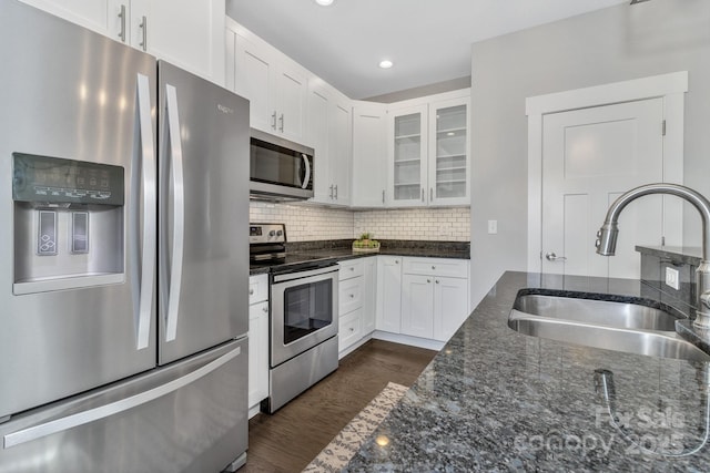 kitchen with appliances with stainless steel finishes, backsplash, sink, dark stone countertops, and white cabinets