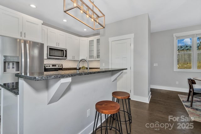 kitchen featuring a kitchen breakfast bar, dark hardwood / wood-style floors, decorative backsplash, decorative light fixtures, and white cabinetry