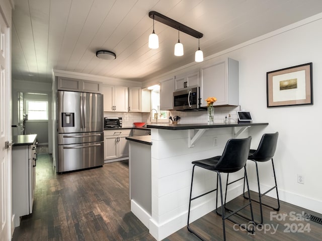 kitchen featuring hanging light fixtures, stainless steel appliances, a kitchen breakfast bar, dark hardwood / wood-style flooring, and kitchen peninsula