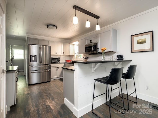 kitchen with dark countertops, a kitchen breakfast bar, tasteful backsplash, stainless steel appliances, and a peninsula