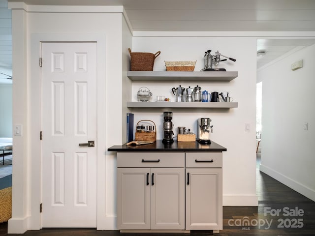 bar with dark wood-type flooring, baseboards, a dry bar, and ornamental molding