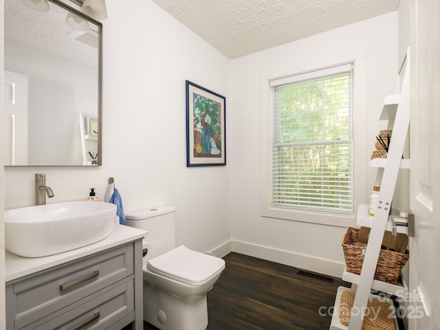 half bath featuring wood finished floors, toilet, vanity, baseboards, and a textured ceiling