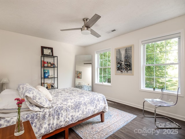 bedroom featuring a ceiling fan, a textured ceiling, baseboards, dark wood-type flooring, and visible vents