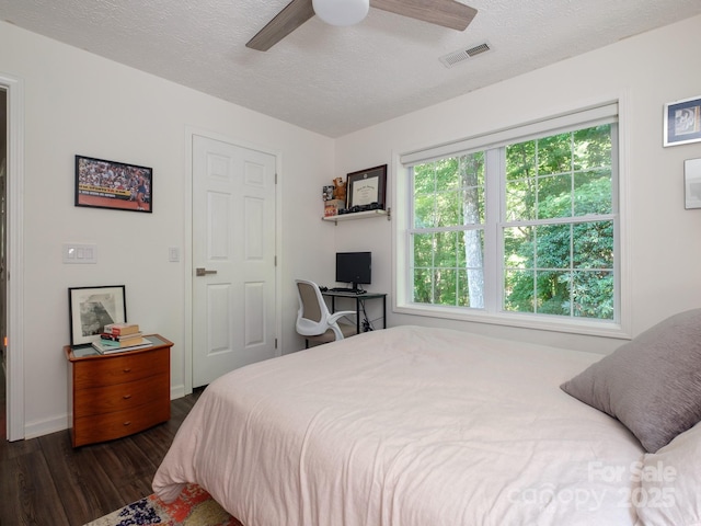 bedroom with a textured ceiling, dark wood finished floors, baseboards, visible vents, and a ceiling fan