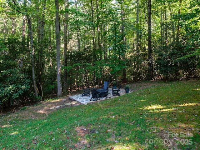 view of yard with a fire pit, a view of trees, and a patio