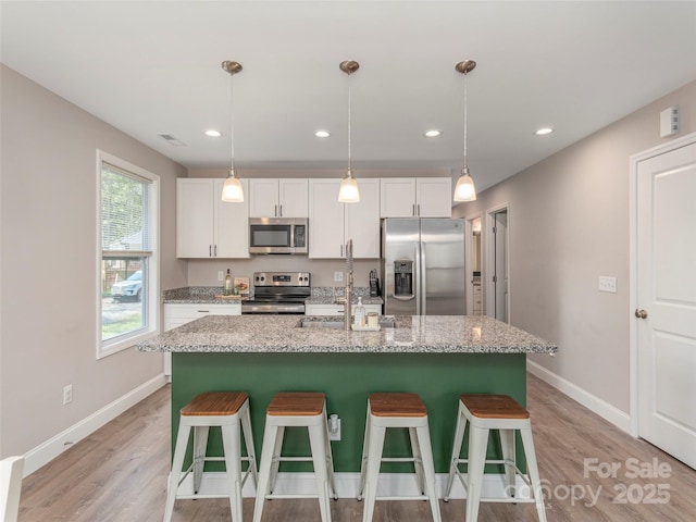 kitchen with white cabinetry, light stone countertops, decorative light fixtures, a center island with sink, and appliances with stainless steel finishes