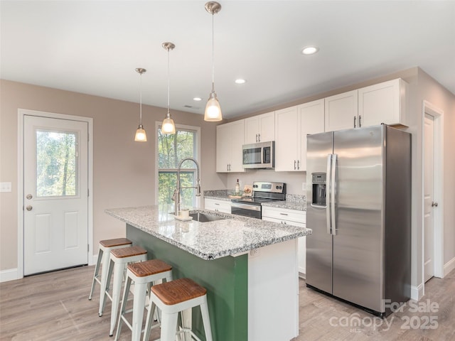 kitchen with light stone countertops, sink, stainless steel appliances, a kitchen island with sink, and white cabinets