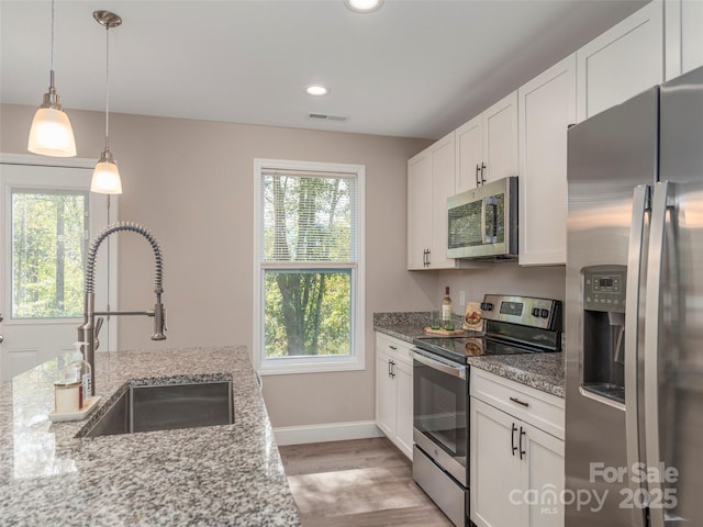 kitchen with light stone countertops, appliances with stainless steel finishes, a healthy amount of sunlight, sink, and white cabinets