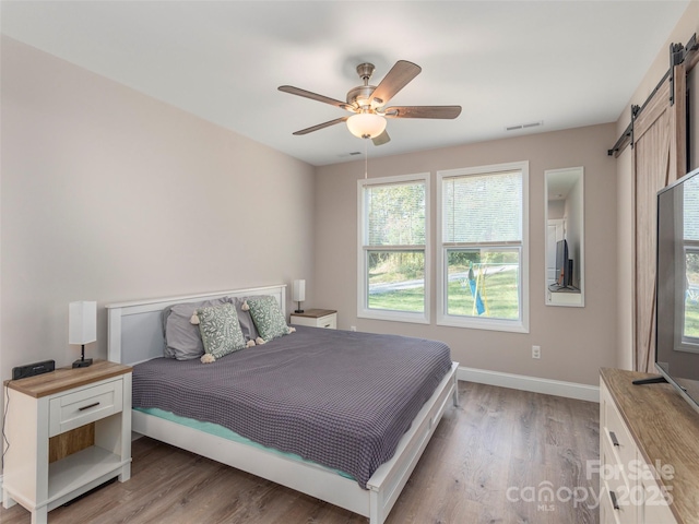 bedroom featuring hardwood / wood-style floors, ceiling fan, and a barn door