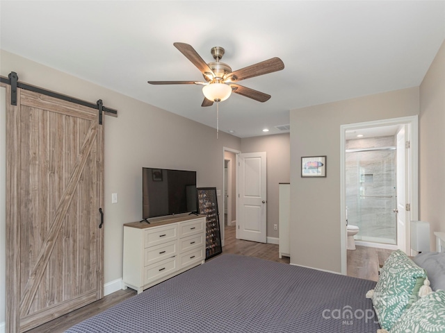 bedroom with connected bathroom, a barn door, ceiling fan, and dark wood-type flooring