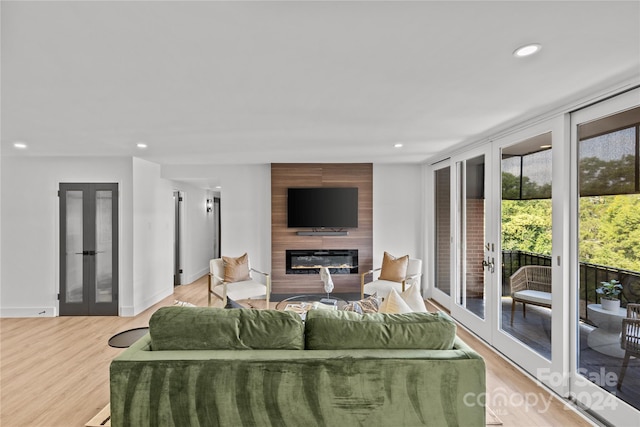 living room featuring french doors, light wood-type flooring, and a large fireplace