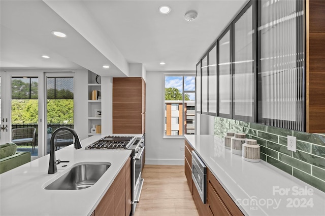 kitchen featuring stainless steel appliances, backsplash, light wood-type flooring, and sink