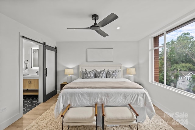 bedroom featuring ceiling fan, sink, wood-type flooring, ensuite bathroom, and a barn door