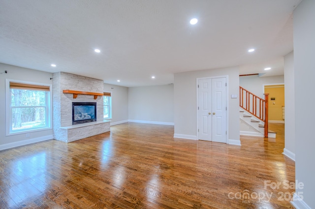 unfurnished living room with a stone fireplace, a wealth of natural light, and light wood-type flooring