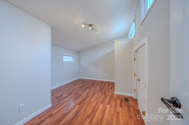 empty room with lofted ceiling, light hardwood / wood-style flooring, and a textured ceiling