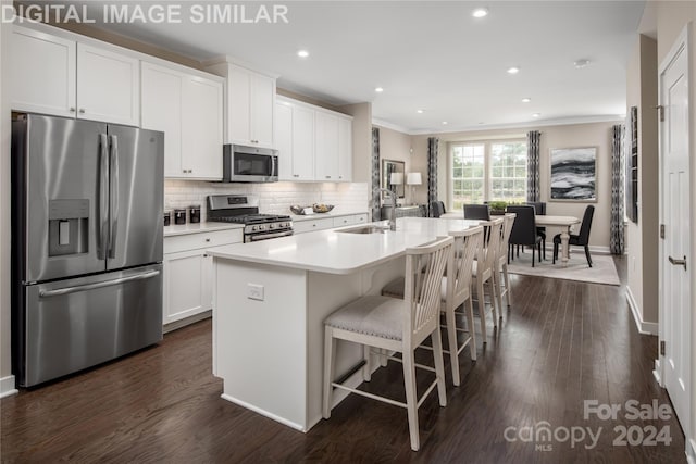 kitchen featuring appliances with stainless steel finishes, an island with sink, sink, white cabinets, and backsplash