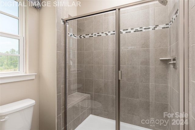 bathroom featuring a shower with door and toilet