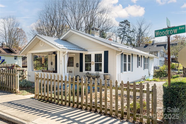 view of front of home featuring a fenced front yard, covered porch, a chimney, and metal roof