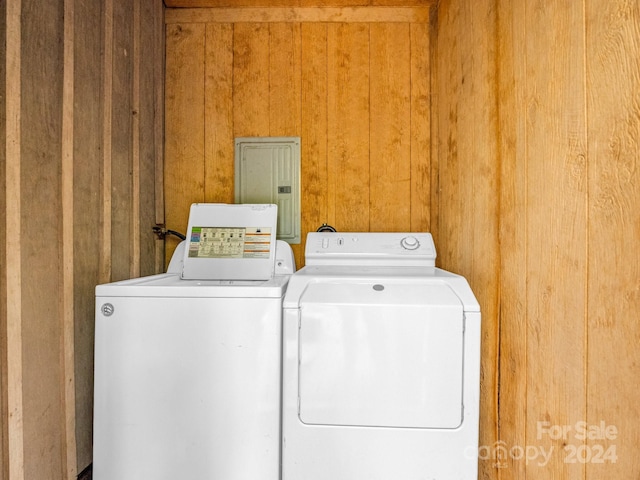 washroom with wood walls, electric panel, and washing machine and dryer