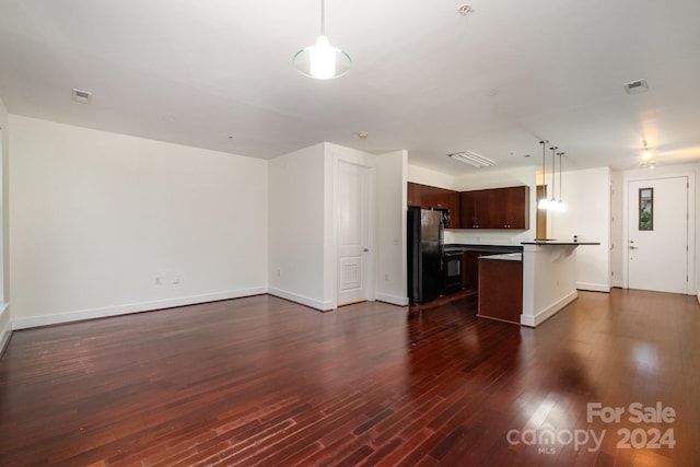 kitchen featuring a kitchen island, black refrigerator, decorative light fixtures, dark wood-type flooring, and a kitchen bar