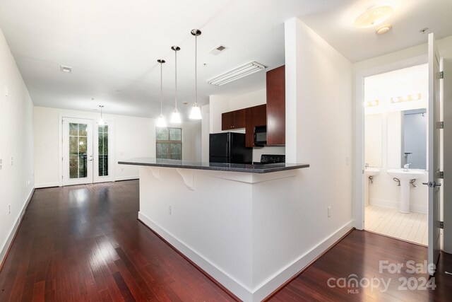 kitchen featuring decorative light fixtures, kitchen peninsula, dark wood-type flooring, and black refrigerator